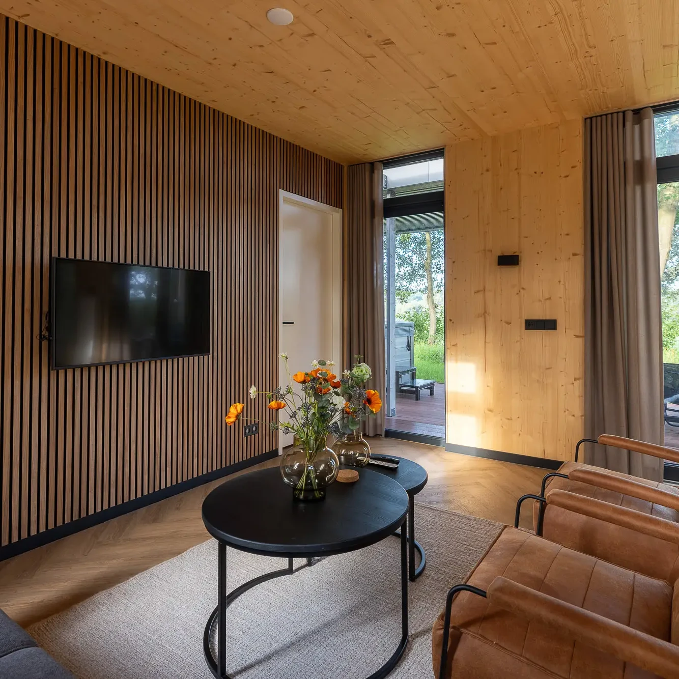 Luxe woonkamer met houten lamellenwand, TV en uitzicht op natuur in Panorama Lodge Markelo