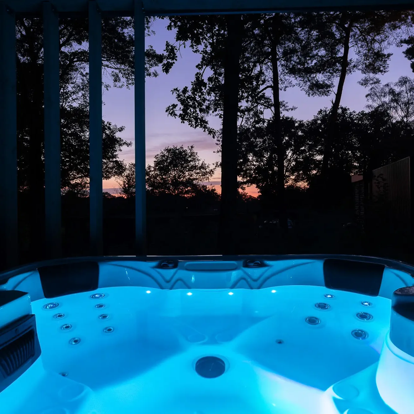 Verlichte jacuzzi met blauw licht bij zonsondergang omringd door bomen in Markelo