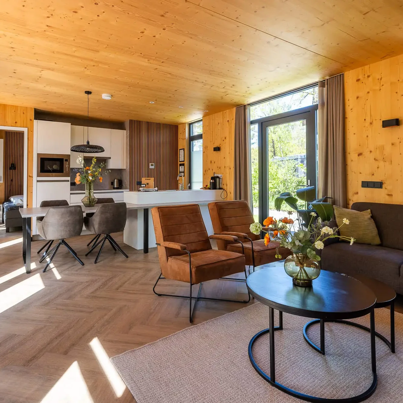 Luxe woonkamer met houten interieur, moderne keuken en grote ramen met uitzicht op natuur in Panorama Lodge Markelo