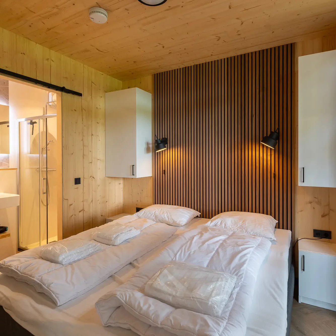 Luxe slaapkamer met houten wanden, slatted headboard en ensuite badkamer in Panorama Lodge Markelo